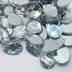 Peut inclure: Un tas de strass en verre transparent en forme de goutte. Les strass ont un design facetté et une finition miroir.