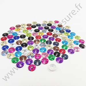 May include: Assortment of colourful iridescent sequins with a hole in the centre. The sequins are arranged in a heart shape on a white background.