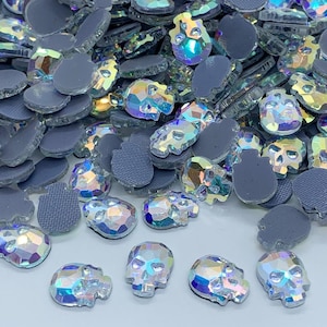 Peut inclure: Une collection de strass irisés en forme de crâne avec un dos plat gris. Les strass ont une surface à facettes qui reflète un arc-en-ciel de couleurs. Ces embellissements décoratifs sont parfaits pour l'artisanat et ajoutent une touche unique.