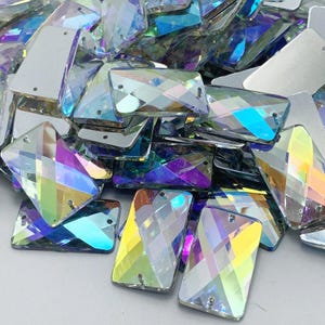 Puede incluir: Un montón de piedras de cristal rectangulares iridiscentes. Las piedras tienen un efecto arcoíris y están esparcidas sobre una superficie blanca.