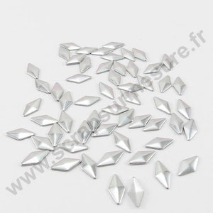 Peut inclure: Un assortiment de clous métalliques en forme de diamant de couleur argent. Les clous sont petits et ont une surface légèrement bombée et brillante.
