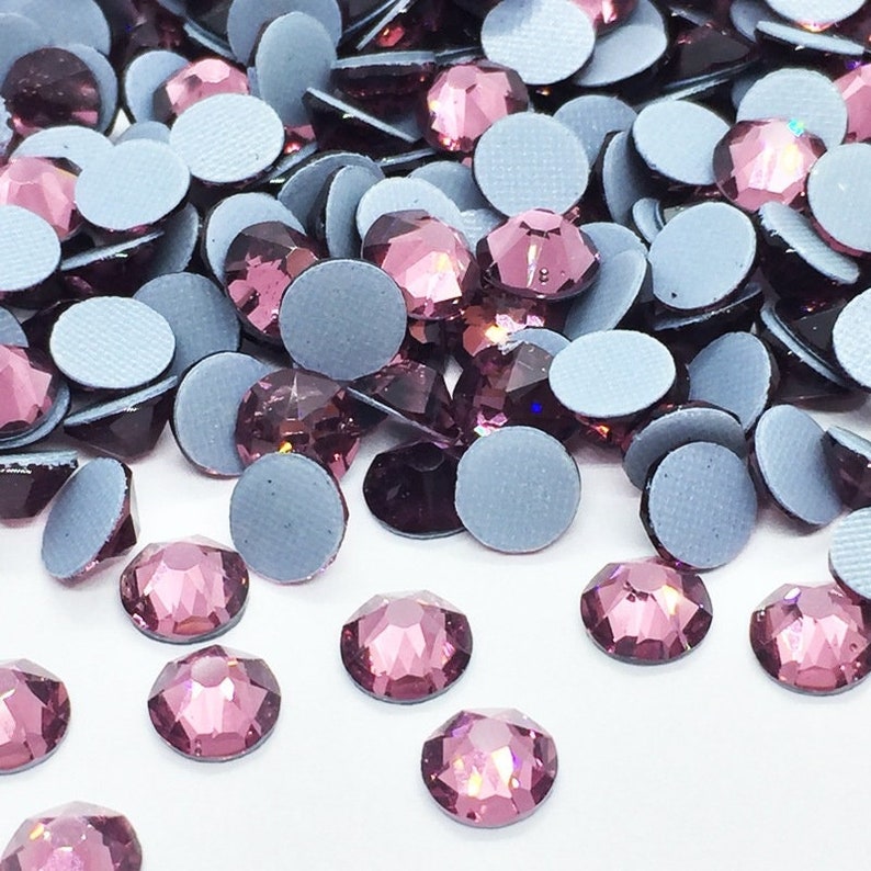 May include: A large quantity of small, round, purple rhinestones with adhesive backing. The rhinestones are scattered on a white surface.