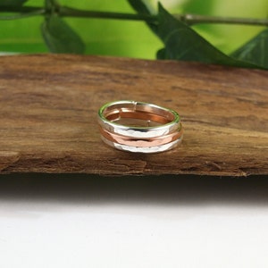 May include: A silver and copper ring with three bands. The ring is made of hammered metal and has a rustic look.