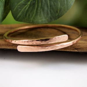 May include: A hammered copper bangle bracelet with a simple, minimalist design. The bracelet is made of two pieces of copper that are joined together at the ends. The bracelet is open ended and can be adjusted to fit most wrists.