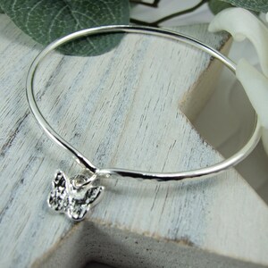 May include: A silver bangle bracelet with a hammered finish and a small butterfly charm.