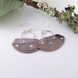 May include: A pair of copper earrings with a silver floral design and silver accents. The earrings are hanging from silver hooks.