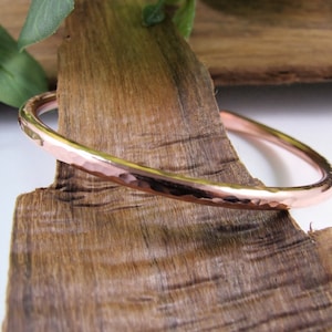 May include: A hammered copper bangle bracelet. The bracelet is a simple, solid band of copper with a hammered finish. It is a classic and timeless piece of jewellery.