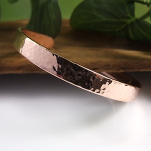 May include: A hammered copper bracelet with a smooth, polished finish. The bracelet is a simple, elegant design that is perfect for everyday wear.