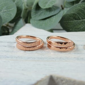 May include: Two copper rings, one with a hammered finish and the other with a textured finish. The rings are both open and are designed to be worn on the finger.