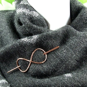 May include: A rose gold infinity symbol scarf pin. The pin is made of wire and has a simple, elegant design.