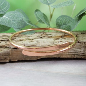 May include: A hammered copper bangle bracelet with a simple, minimalist design. The bracelet is open and adjustable to fit most wrists.