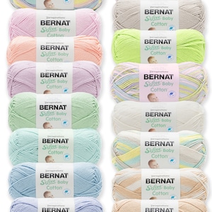 May include: A collection of 12 skeins of Bernat Softee Baby Cotton yarn in various pastel colors. Each skein has a label with the brand name and yarn type.