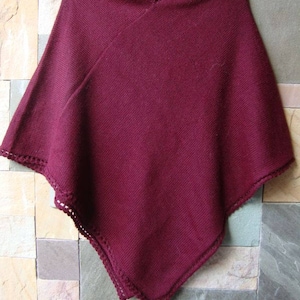 Pode incluir: Um poncho de malha bord&ocirc; com uma borda de croch&ecirc;. O poncho est&aacute; pendurado em um cabide contra uma parede de azulejos.