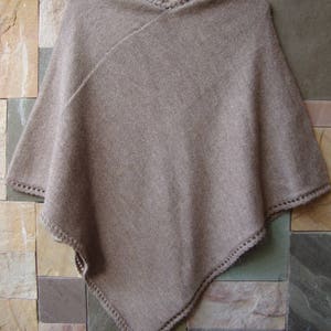 Pode incluir: Um poncho de malha marrom com uma borda de croch&ecirc;. O poncho &eacute; feito de um material macio e leve e tem um caimento solto.