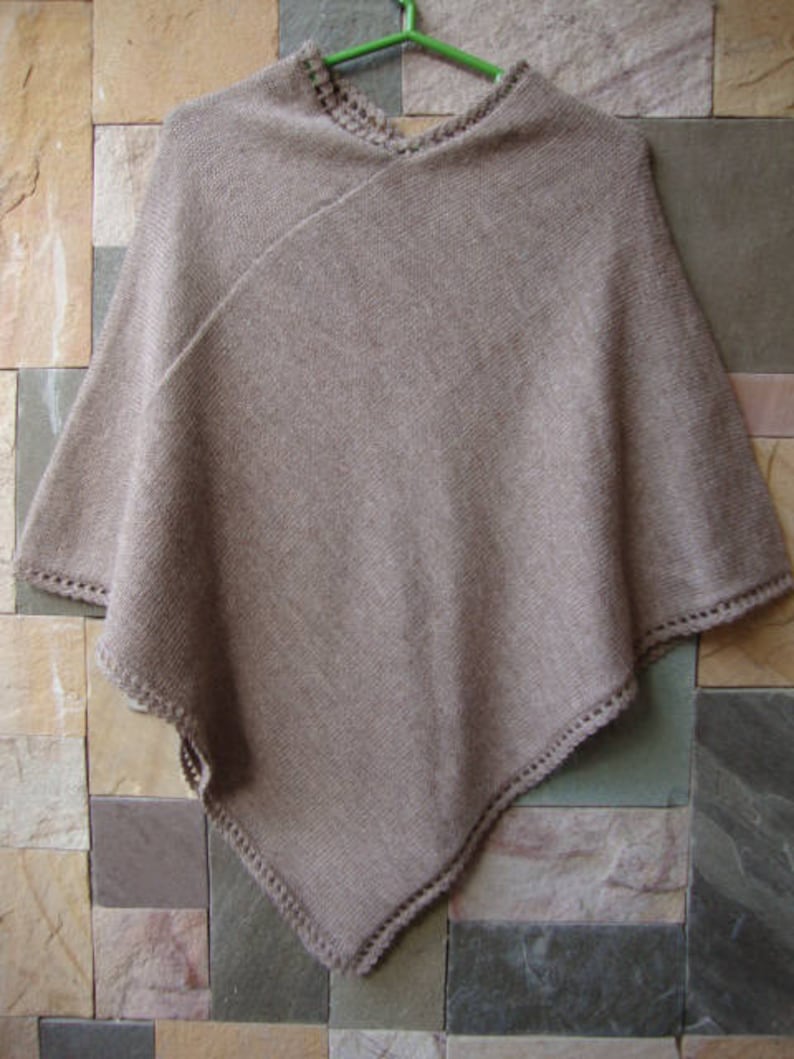 Pode incluir: Um poncho de malha marrom com uma borda de croch&ecirc;. O poncho &eacute; feito de um material macio e leve e tem um caimento solto.