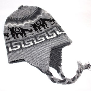May include: Gray knit hat with ear flaps and a braided tassel. The hat features a repeating pattern of black elephants and white geometric shapes against a gray background. A cozy winter accessory.