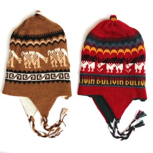 May include: Two knitted alpaca hats. One is brown with llama designs, the other is red with a geometric pattern and the text "Bolivia". Both have ear flaps and tassels. These hats are perfect for cold weather.