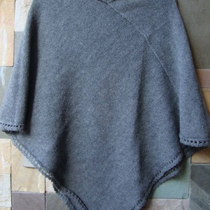 Pode incluir: Poncho de malha cinzenta com acabamento em croch&ecirc; em torno do decote e das bordas.