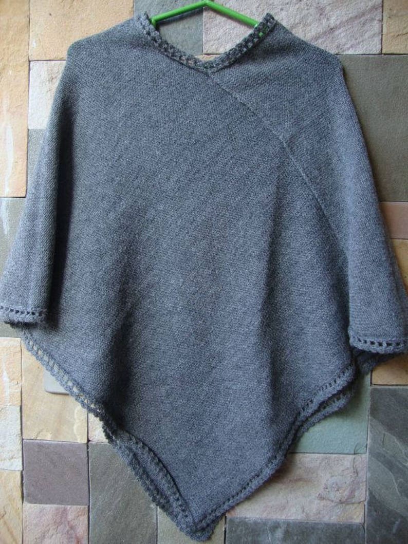 Pode incluir: Poncho de malha cinzenta com acabamento em croch&ecirc; em torno do decote e das bordas.