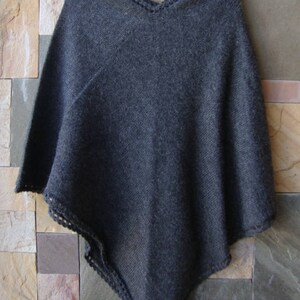 Pode incluir: Um poncho de malha cinza escuro com uma borda de croch&ecirc;. O poncho &eacute; feito de um material macio e quente e tem um caimento solto.