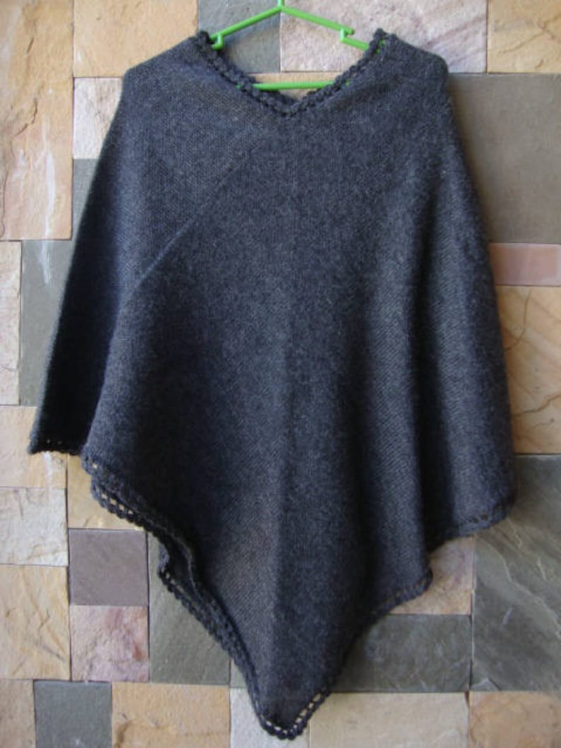 Pode incluir: Um poncho de malha cinza escuro com uma borda de croch&ecirc;. O poncho &eacute; feito de um material macio e quente e tem um caimento solto.