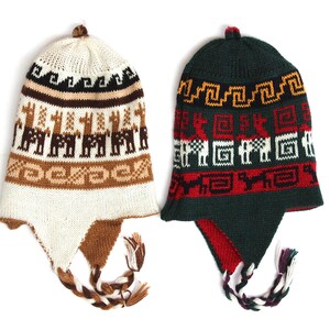 May include: Two knitted winter hats with ear flaps. One is cream-colored with brown llama patterns and the other is dark green with red and white geometric designs. Both have braided ties.