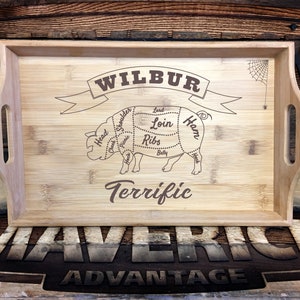 May include: A wooden serving tray with a pig cut-out design and the words "Wilbur Terrific" engraved on it. The pig is labeled with different cuts of meat, including "Ham", "Loin", and "Ribs".