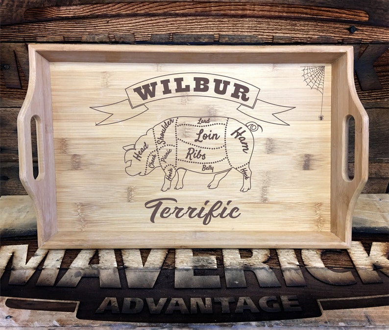 May include: A wooden serving tray with a pig cut-out design and the words "Wilbur Terrific" engraved on it. The pig is labeled with different cuts of meat, including "Ham", "Loin", and "Ribs".