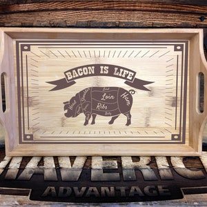 May include: A wooden serving tray with a brown border and a pig illustration. The pig is labeled with different cuts of meat, including "Bacon is Life". The tray is made by Maverick Advantage.