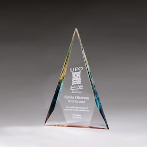 May include: A clear glass pyramid award with a blue, yellow, and orange gradient. The award has the text "UFO" and "Wonder Forty Organization" engraved on it. The award also has the text "Sylvia Ottersen RPS Portland" and "In grateful appreciation of your hard work and dedication" engraved on it. The award also has the text "President 2018-2019" engraved on it.