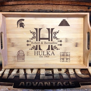 May include: A personalized wooden serving tray with a brown engraved design. The tray features a large letter "H" with a leafy design, the names "Robert & Bernadine", the last name "Hulka", and the year "Est. 1965". The tray also features a Spartan helmet, a pyramid, a silo, and a quilt block.