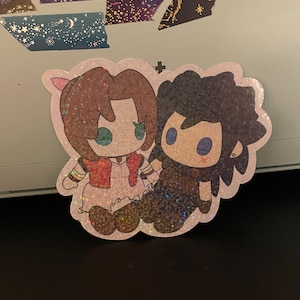 May include: A glittery sticker featuring two cartoon characters holding hands. One character wears a red top and the other has dark hair. The sticker has a sparkly, iridescent finish and a white border.