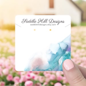 May include: White card with blue and purple watercolour-style design. The text "Saddle Hill Designs" and "saddlehilldesigns.etsy.com" is printed on the card.