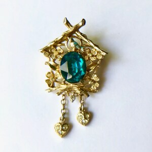 May include: Gold tone cuckoo clock brooch with a green jewel and dangling heart charms.
