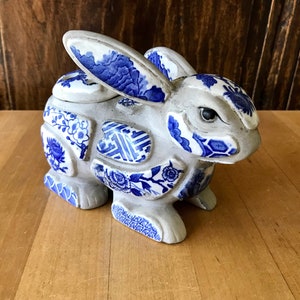 May include: A ceramic rabbit sculpture made of blue and white porcelain tiles. The rabbit is standing on a wooden surface.