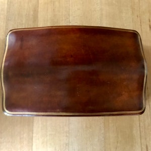 May include: A brown leather footstool with a gold trim around the edge.