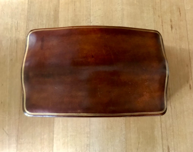 May include: A brown leather footstool with a gold trim around the edge.