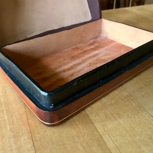 May include: A wooden box with a black and brown trim. The box is open and the inside is lined with a brown material.