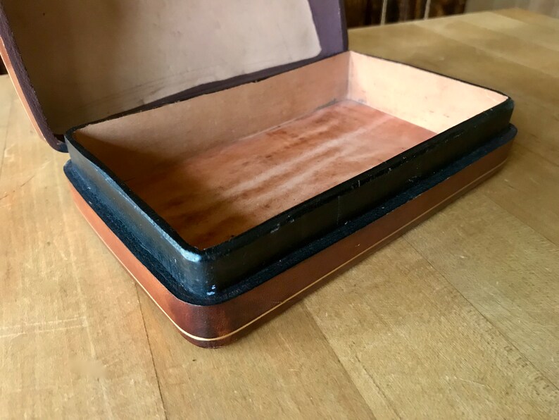 May include: A wooden box with a black and brown trim. The box is open and the inside is lined with a brown material.