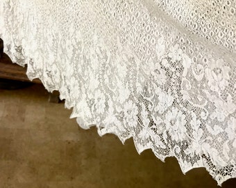 May include: White lace fabric with a delicate floral pattern. The lace has a scalloped edge.