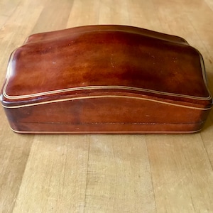 May include: A brown leather box with a curved top and gold trim. The box is closed.