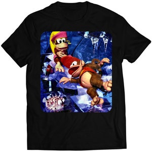 Puede incluir: Una camiseta negra con una imagen colorida de Donkey Kong y Diddy Kong del videojuego Donkey Kong Country. La imagen muestra a los dos personajes en un entorno nevado y helado.