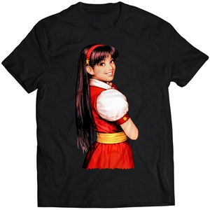 Könnte beinhalten: Schwarzes T-Shirt mit einer bunten Illustration einer Frau mit langen dunklen Haaren, die ein rotes Kleid mit einem gelben Gürtel und einem weißen Kragen trägt.
