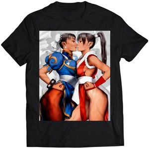 Może przedstawiać: Czarny T-shirt z nadrukiem graficznym przedstawiającym dwie kobiety w pozach walki. Kobieta po lewej stronie ma na sobie niebiesko-biały strój, a kobieta po prawej stronie ma na sobie czerwono-biały strój. Obie patrzą na siebie z intensywnymi wyrażeniami twarzy.