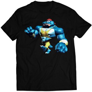 Puede incluir: Camiseta negra con un cocodrilo azul musculoso de dibujos animados que lleva un pañuelo rojo y pantalones cortos amarillos. El cocodrilo está en posición de lucha.