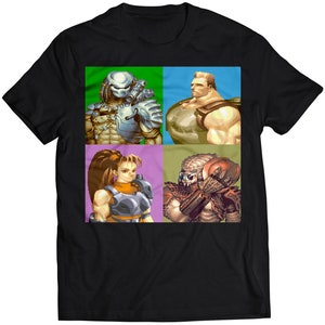 Könnte beinhalten: Ein schwarzes T-Shirt mit einem pixeligen Bild von vier Charakteren aus einem Videospiel. Die Charaktere sind ein grüner und brauner Außerirdischer, ein grüner und brauner Predator, eine Frau mit braunen Haaren und einem grün-braunen Anzug und ein Mann mit braunen Haaren und einem grün-braunen Anzug.