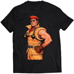Könnte beinhalten: Ein schwarzes T-Shirt mit einer Cartoon-Illustration eines muskulösen Mannes, der eine rote Baskenmütze, ein gelbes Hemd und einen braunen Gürtel trägt. Er hält in jeder Hand eine Granate.