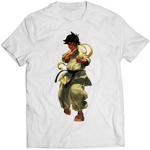 May include: White t-shirt with a graphic of a young man in a karate uniform with a black belt and a yellow sash. The man is in a fighting stance with his right hand raised.