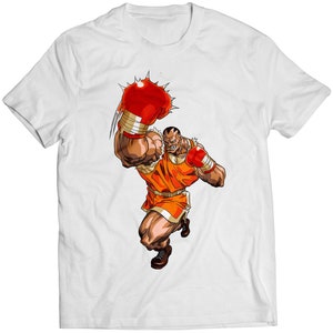 May include: White t-shirt featuring a cartoon illustration of a muscular boxer in an orange outfit and red boxing gloves. The boxer is in a dynamic pose, with one fist raised. The design is centered on the shirt.
