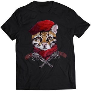 Może przedstawiać: Czarny T-shirt z grafiką kota w czerwonym berecie trzymającego dwie skrzyżowane pistolety.